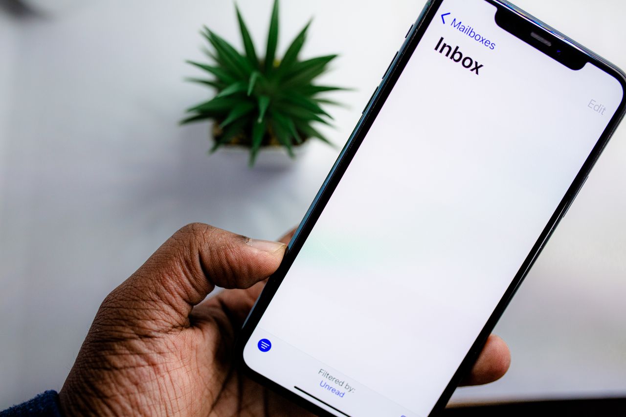 Vue rapprochée d’un écran de smartphone affichant la boîte de réception des e-mails, tenu dans la main d’un adulte.